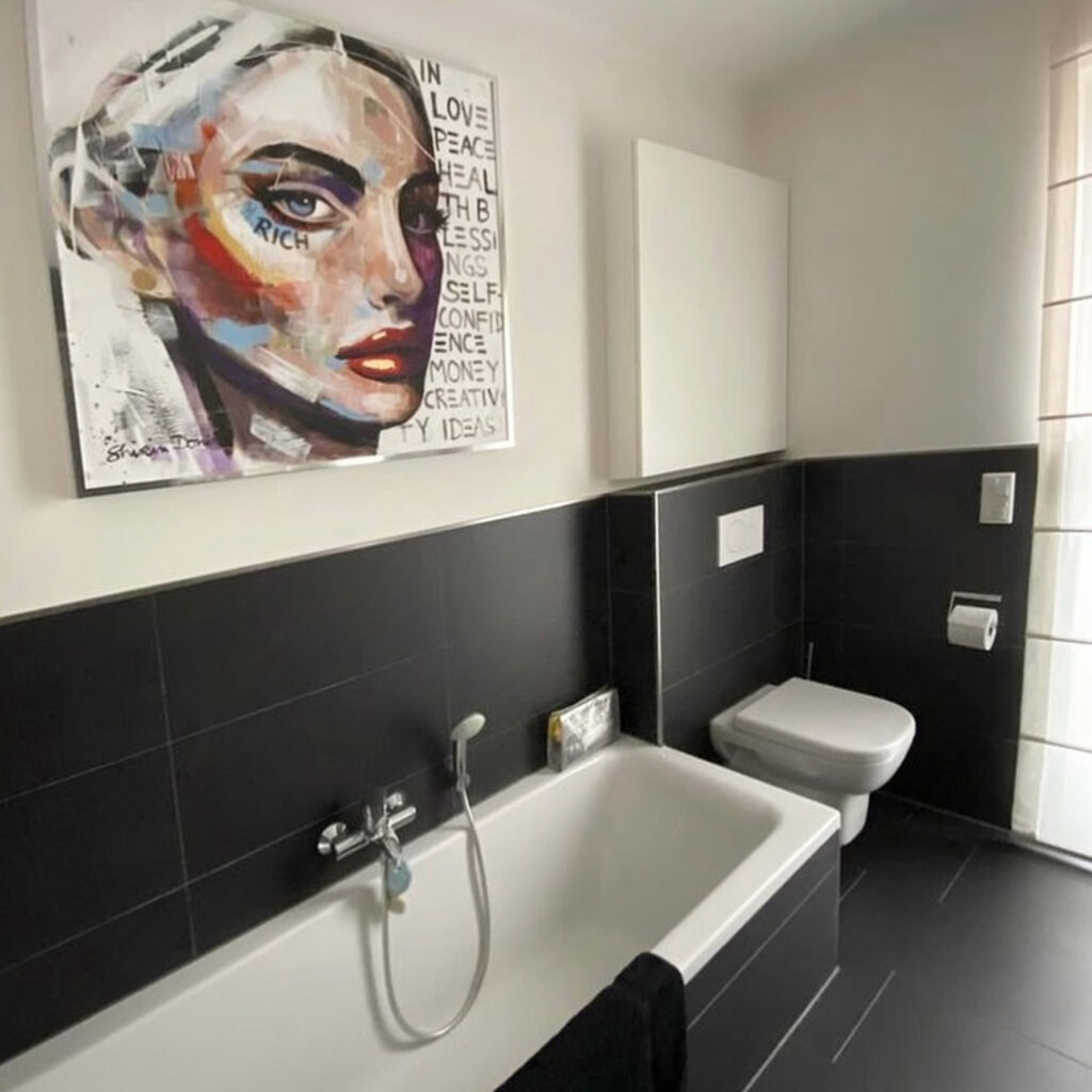 Buntes Kunstwerk mit Frauengesicht und Schriftzügen im Badezimmer über der Badewanne
