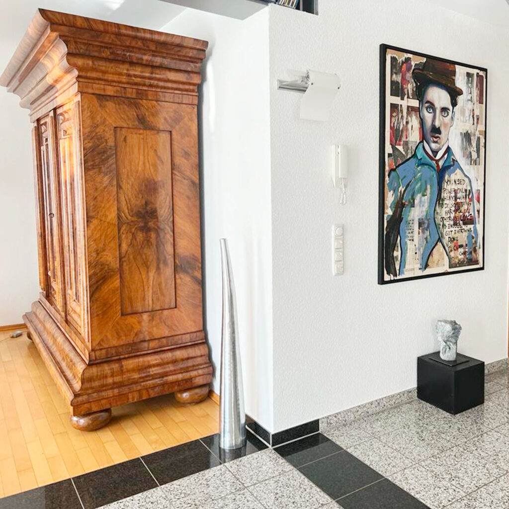Gemälde von Charlie Chaplin im Collage-Stil neben antikem Holzschrank