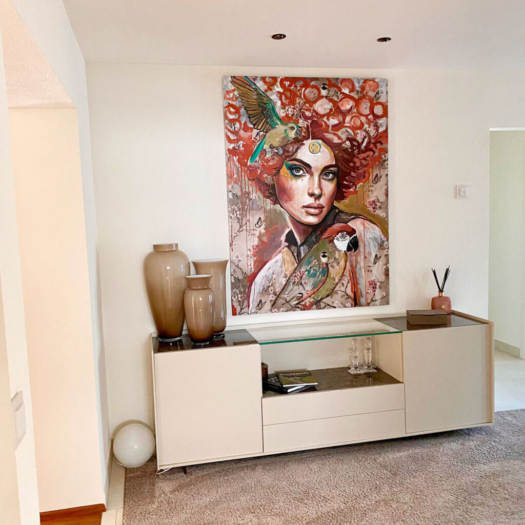 Kunstwerk mit rothaariger Frau und Vögeln über beigem Sideboard
