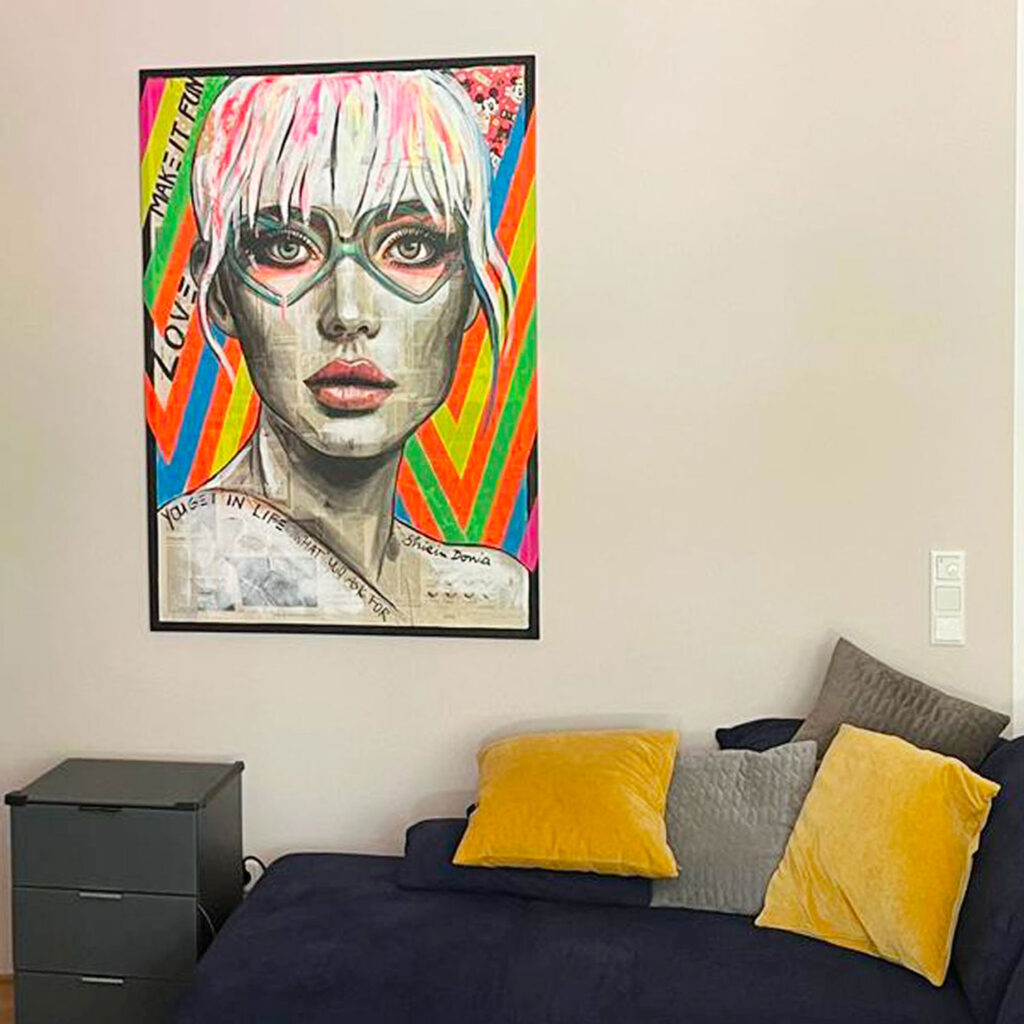 Buntes Pop-Art-Porträt „Make it fun“ über dunkelblauem Sofa im Schlafzimmer